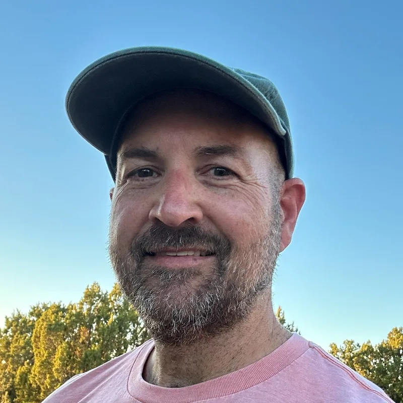 Photo of Jonathan Sandmel smiling outdoors in a green cap